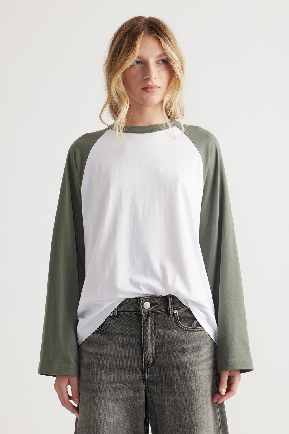 Woman wearing relaxed fit white tee with olive green raglan long sleeves and faded black high waist jeans