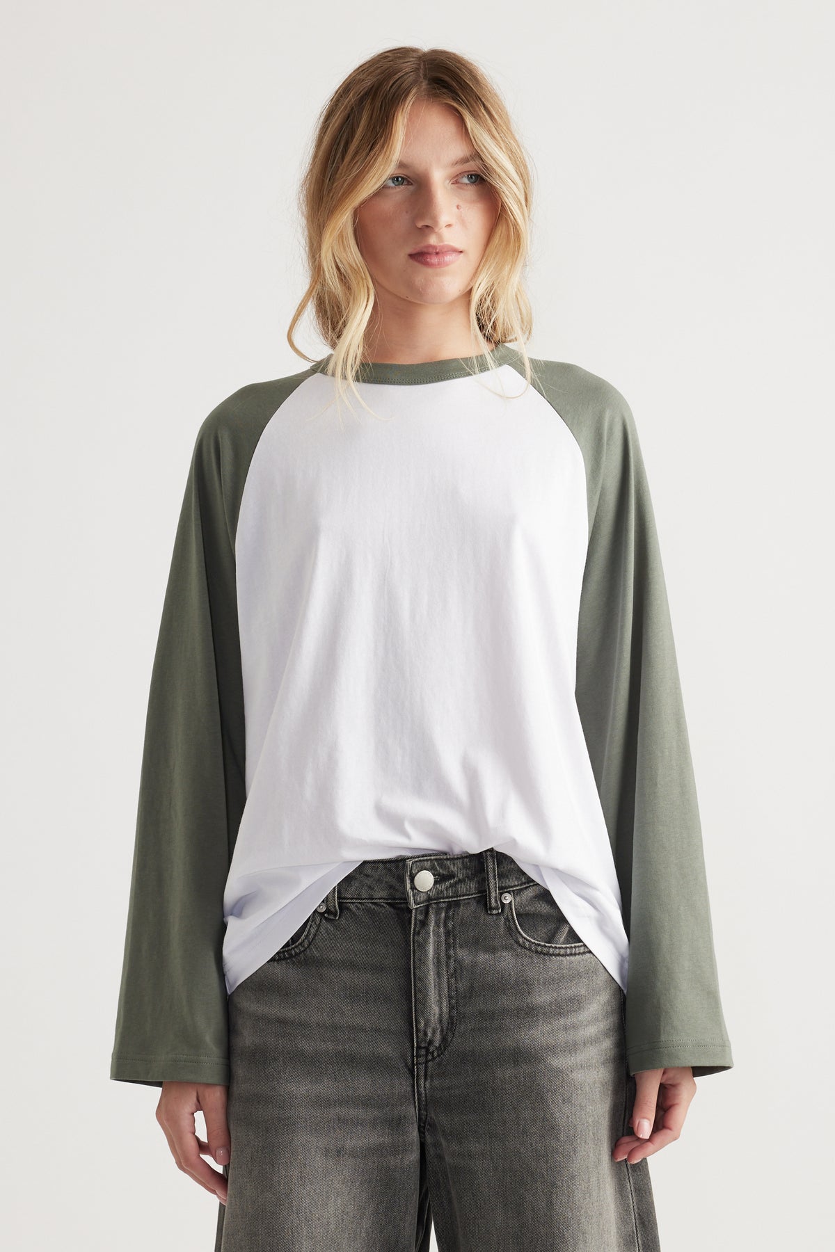 Woman wearing relaxed fit white tee with olive green raglan long sleeves and faded black high waist jeans