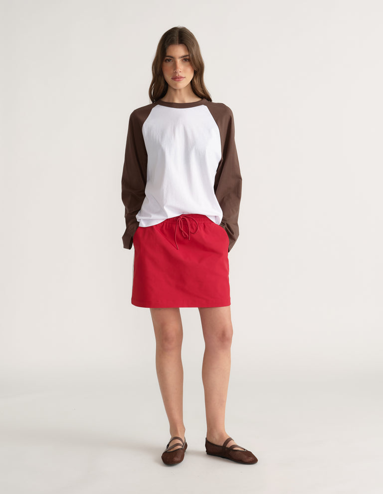 Woman wearing a white and brown raglan long sleeve tee with a red drawstring skirt and sandals