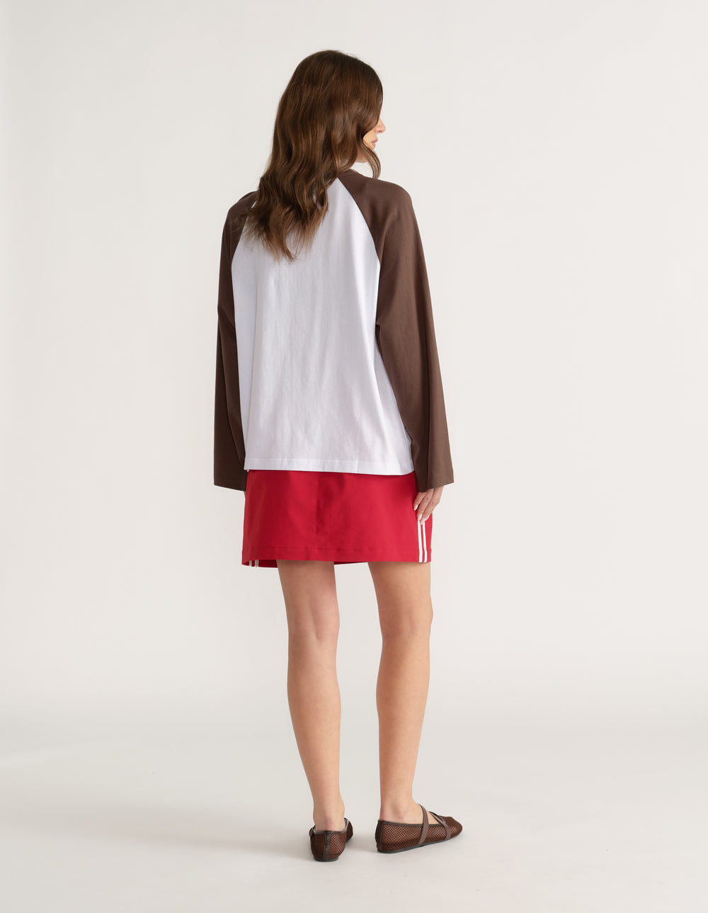 Woman viewed from behind wearing a white and brown raglan long sleeve tee with red shorts and sandals