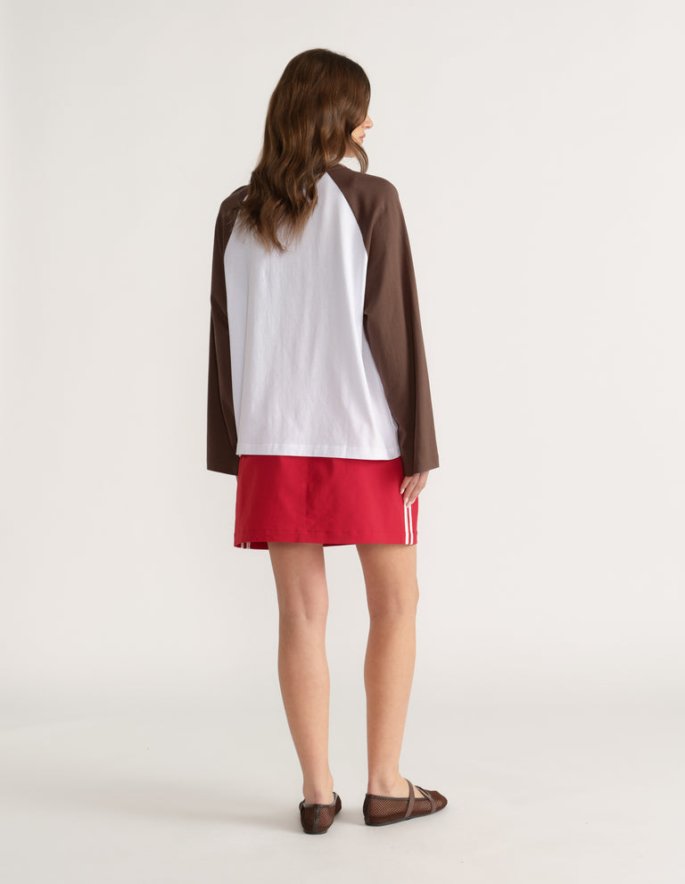 Woman viewed from behind wearing a white and brown raglan long sleeve tee with red shorts and sandals