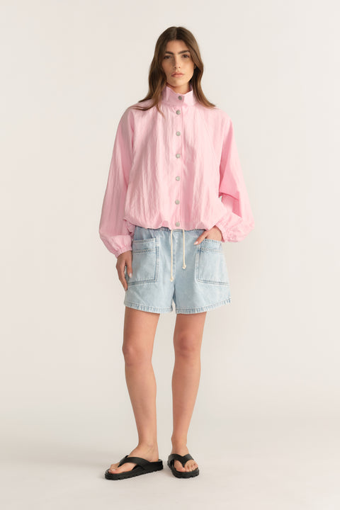 Woman wearing a pink button front shirt with light denim pull on shorts and black sandals