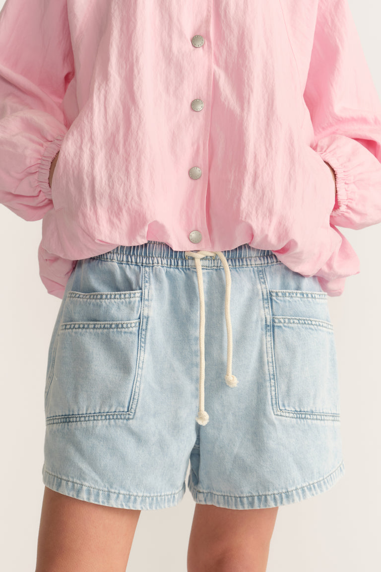 Woman wearing light wash denim shorts with an elastic waist and drawstring, paired with a pink blouse