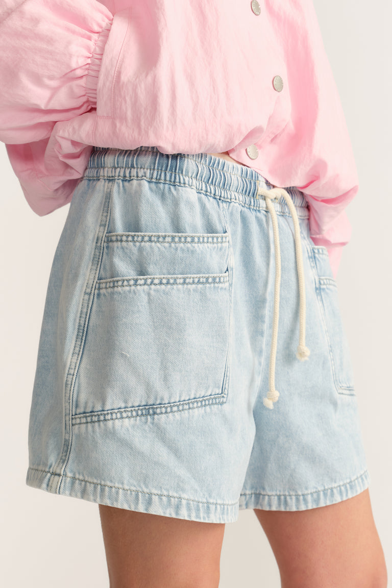 Woman wearing light blue denim shorts with an elastic drawstring waist and pink blouse