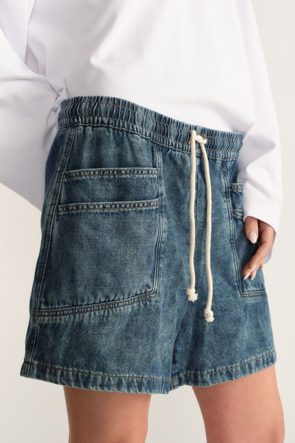 Woman wearing blue denim pull on shorts with an elastic waist, drawstring and utility pockets