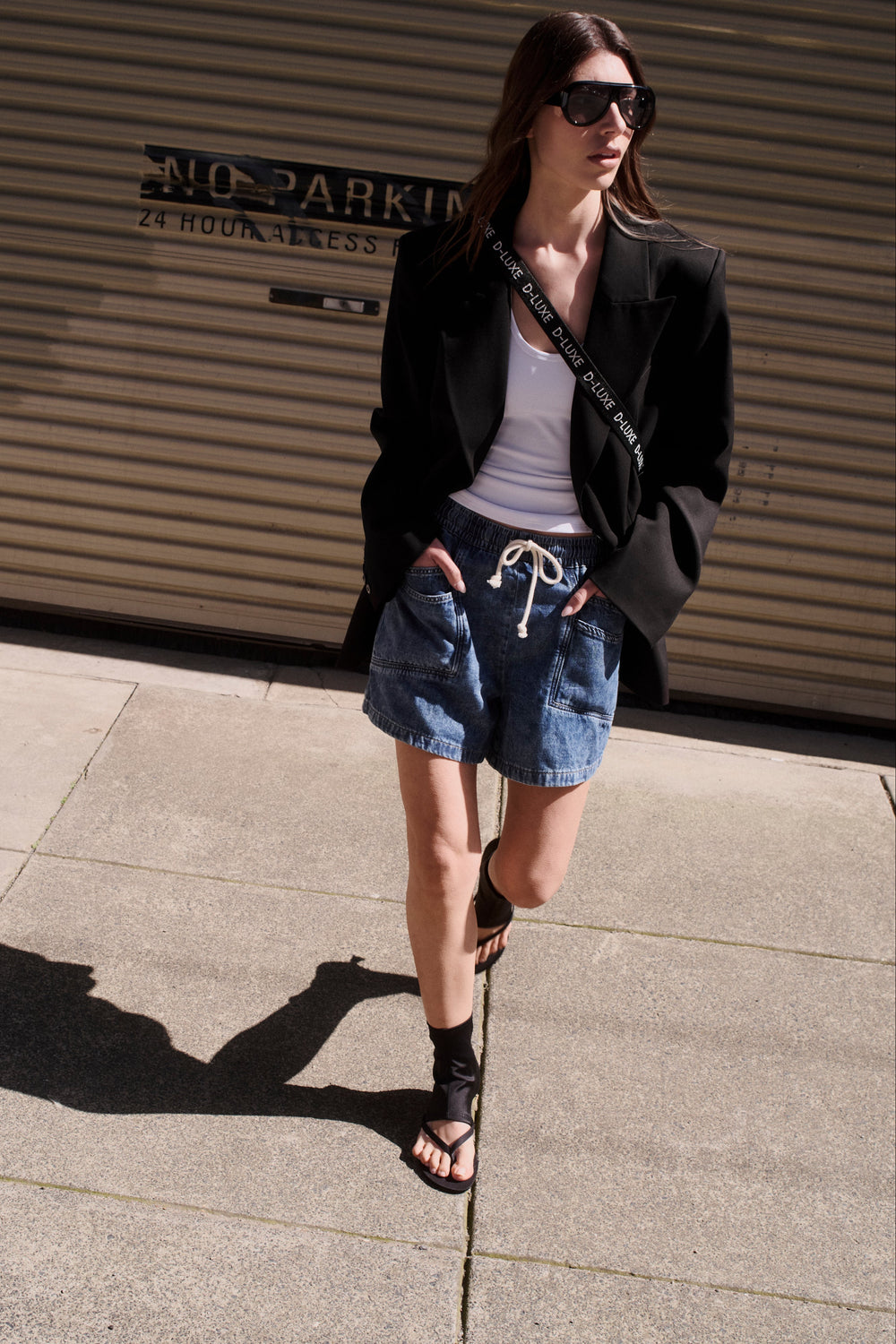 Model wearing a black blazer, white top and relaxed denim shorts with a drawstring waist