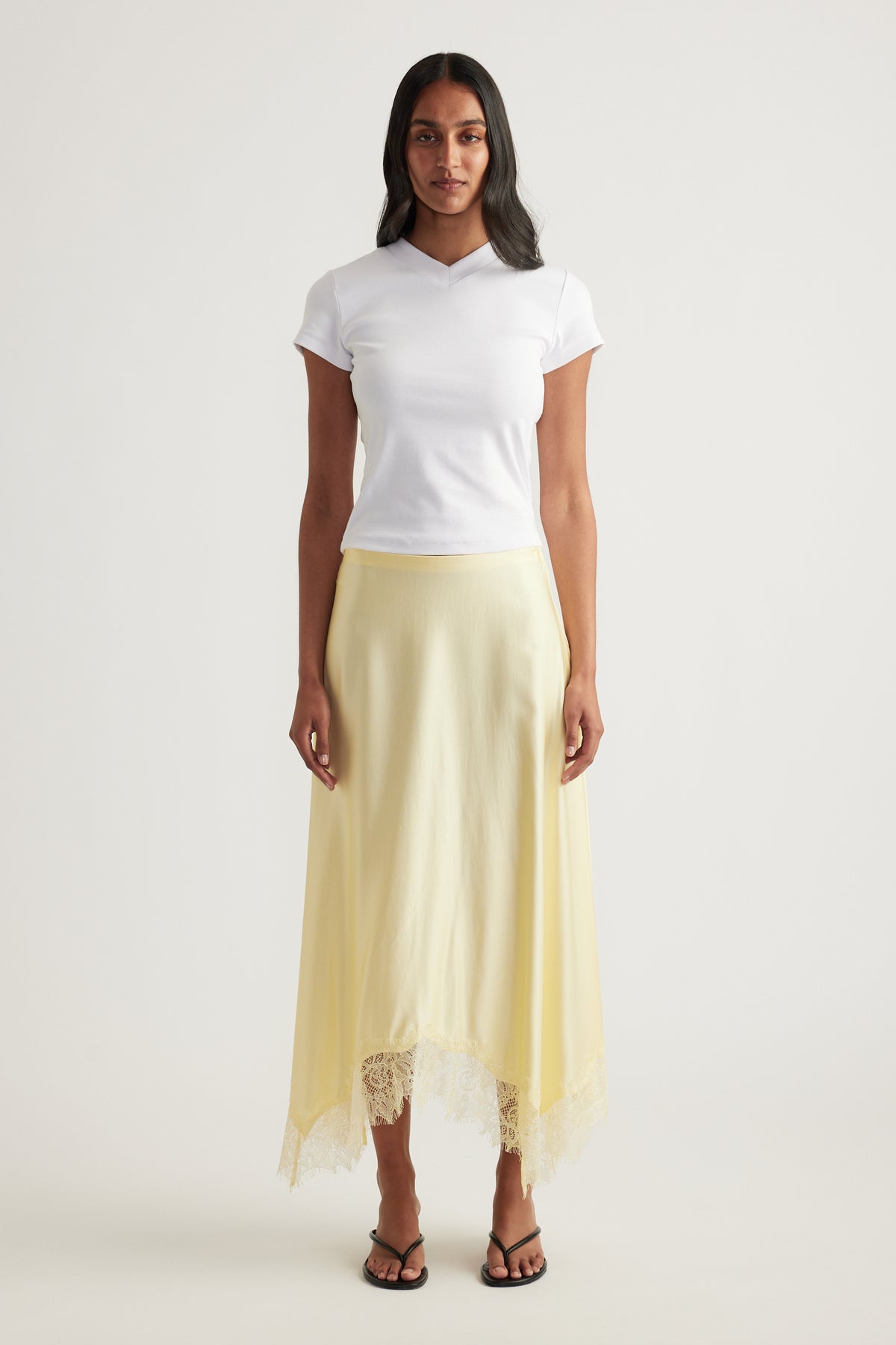 Woman wearing a pale yellow satin midi skirt with lace trim hem and white top