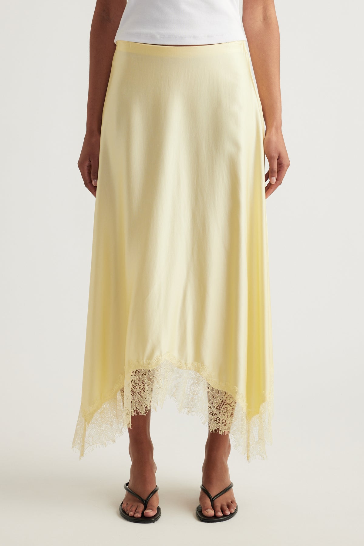 Woman wearing a yellow satin midi skirt with lace trim and handkerchief hem, styled with a white top and sandals