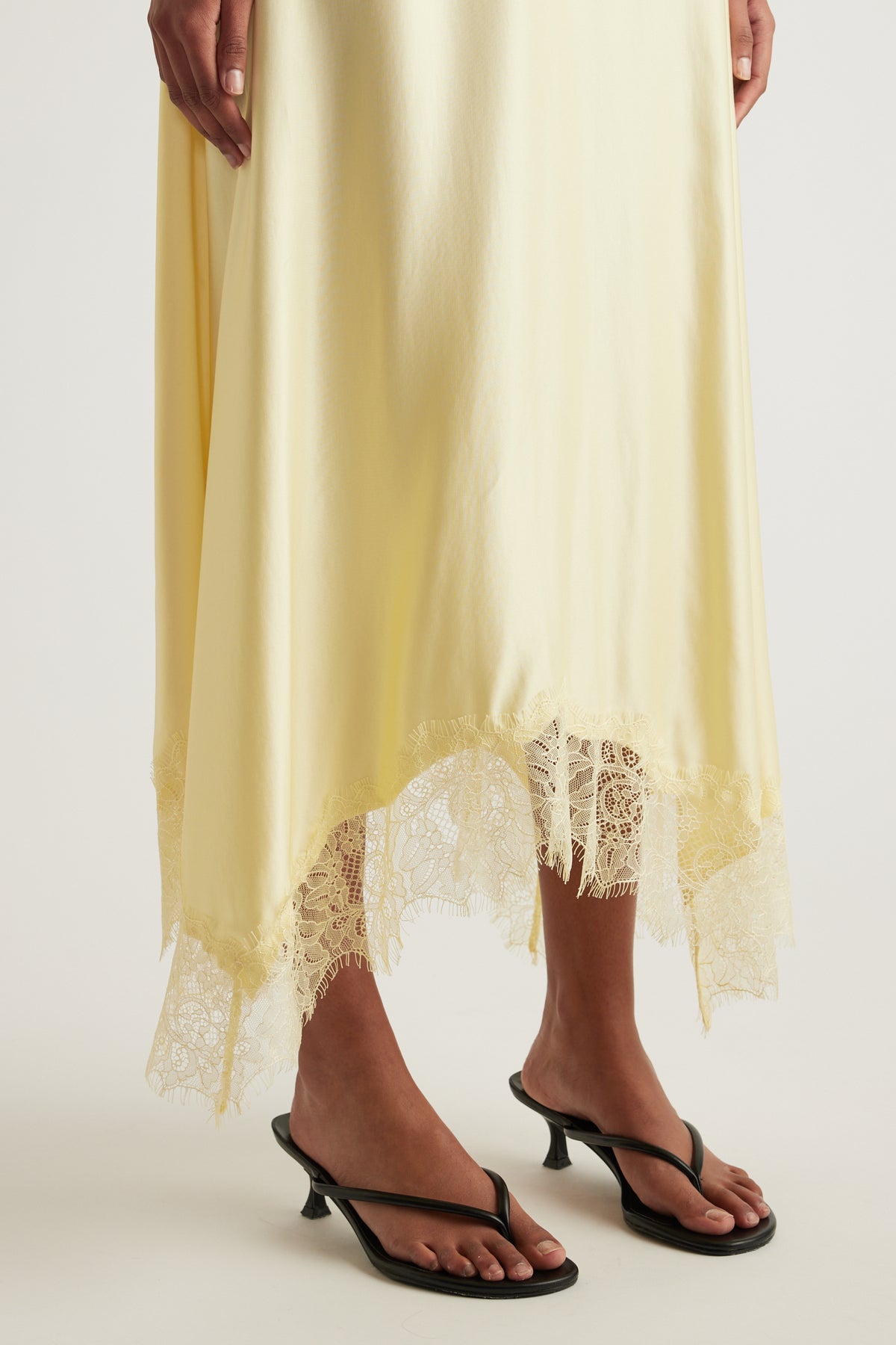 Pale yellow satin midi skirt with lace trim handkerchief hem styled with black heeled sandals