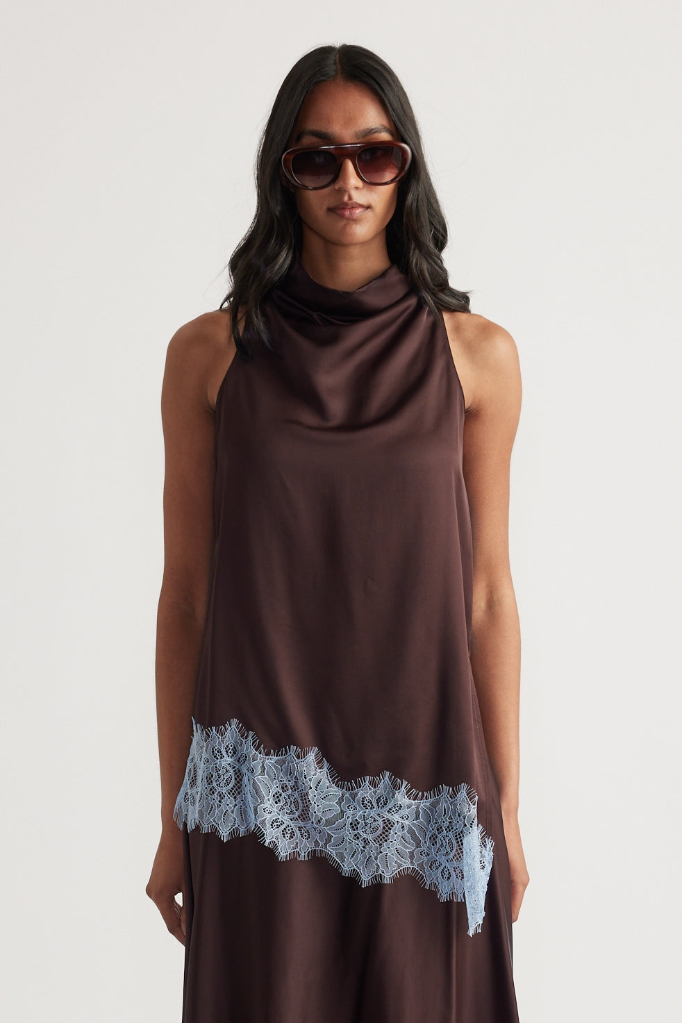Woman wearing a chocolate brown sleeveless cowl neck top with lace trim asymmetric hem and sunglasses