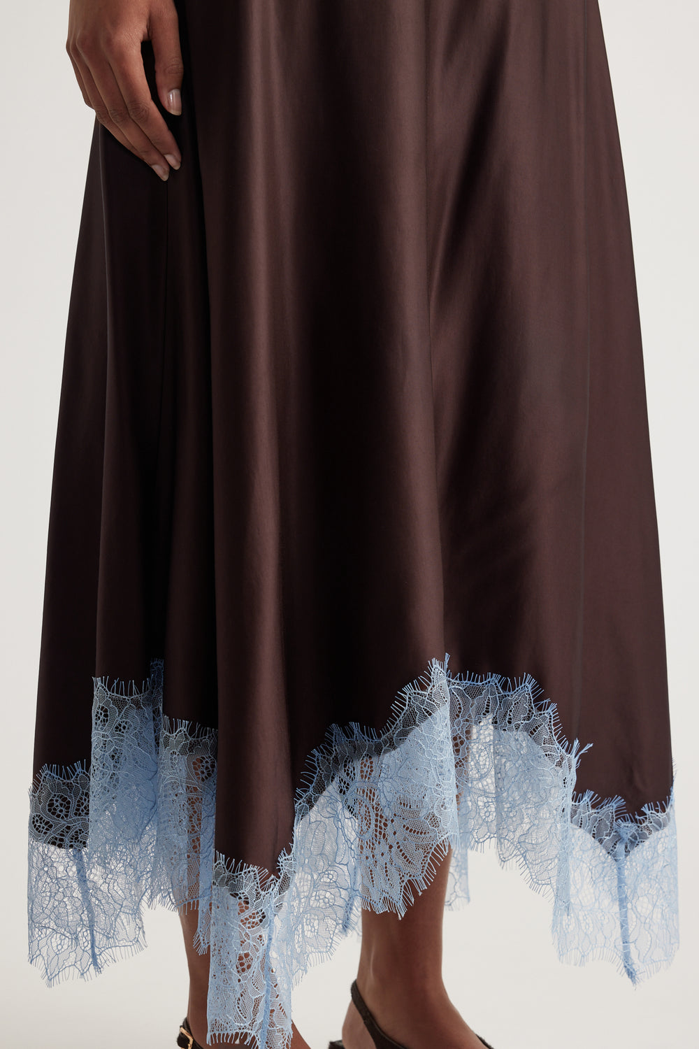 Close view of a woman wearing a chocolate brown satin midi skirt with blue lace trim and a handkerchief hem