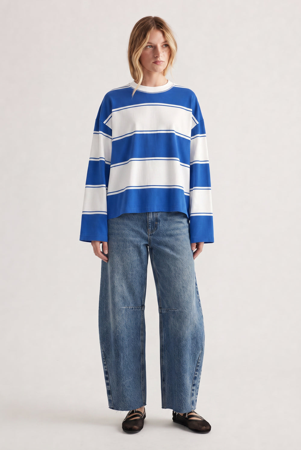 Woman wearing a relaxed long sleeve striped tee in blue and white paired with wide-leg denim jeans and black flats