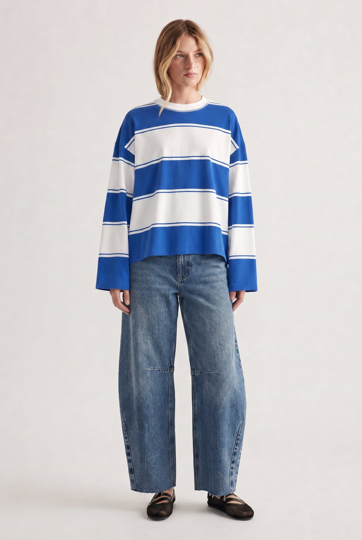 Woman wearing a relaxed long sleeve striped tee in blue and white paired with wide-leg denim jeans and black flats
