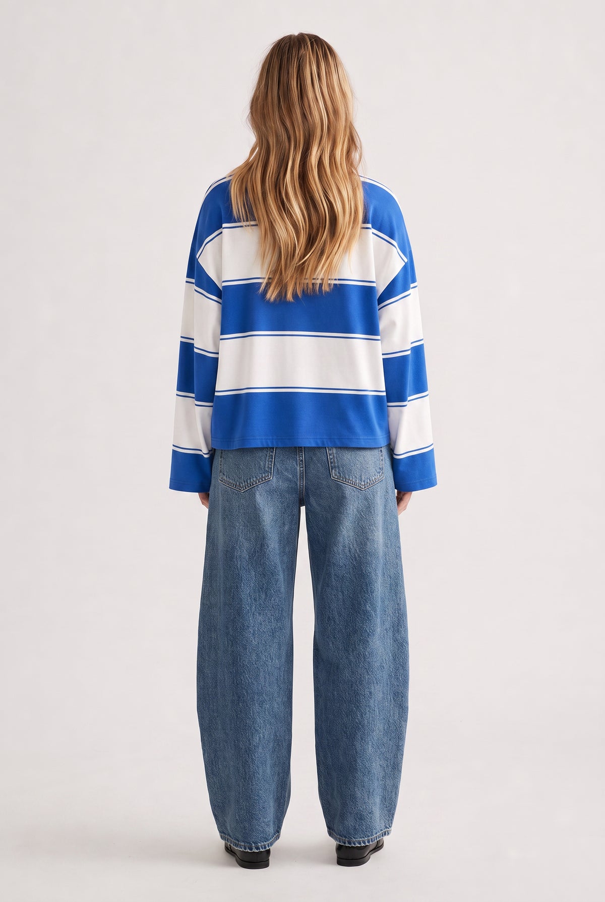 Woman wearing a relaxed-fit blue and white striped long sleeve tee paired with loose dark blue denim jeans