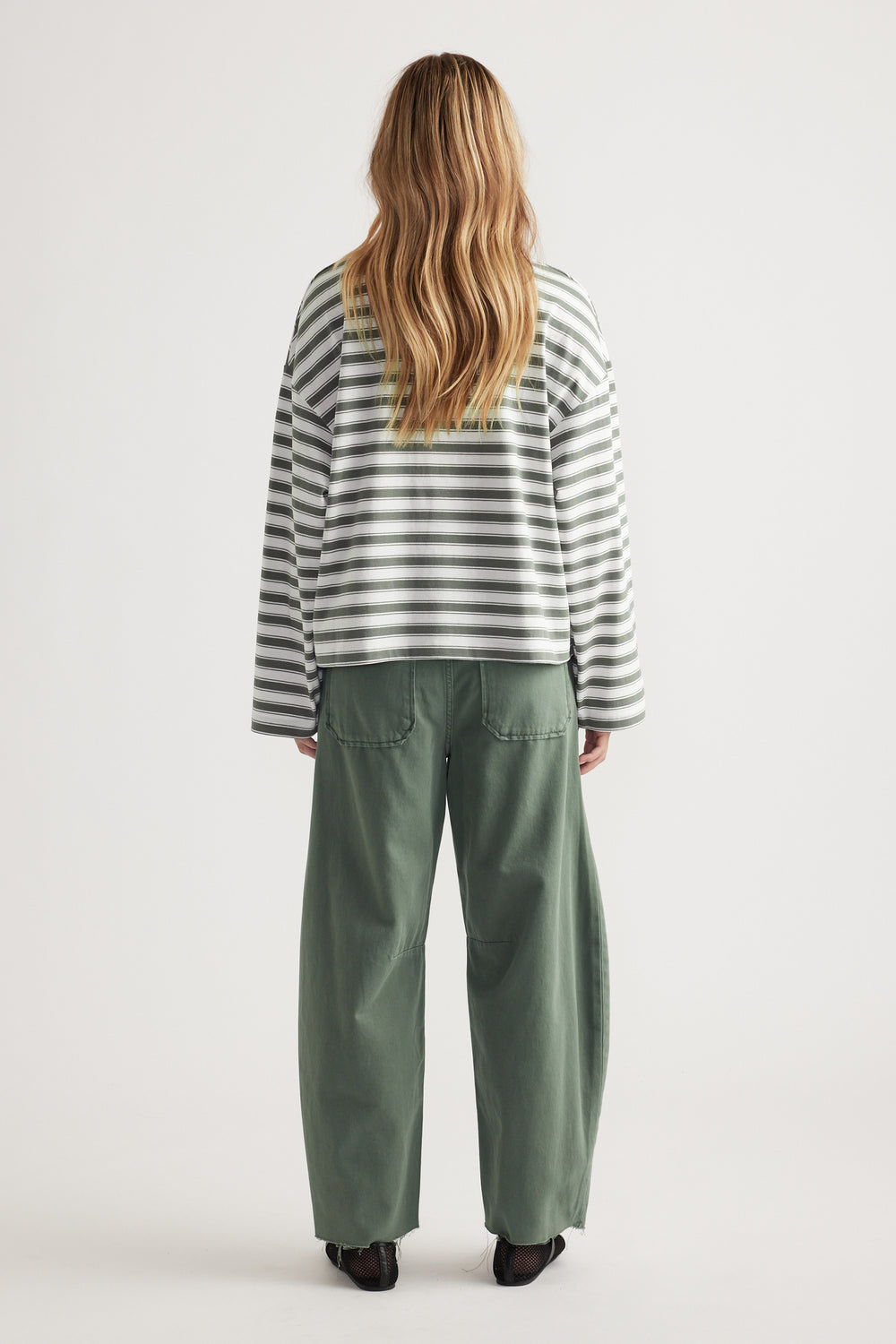 Woman wearing relaxed fit green wide-leg pants and long sleeve white and grey striped tee seen from back