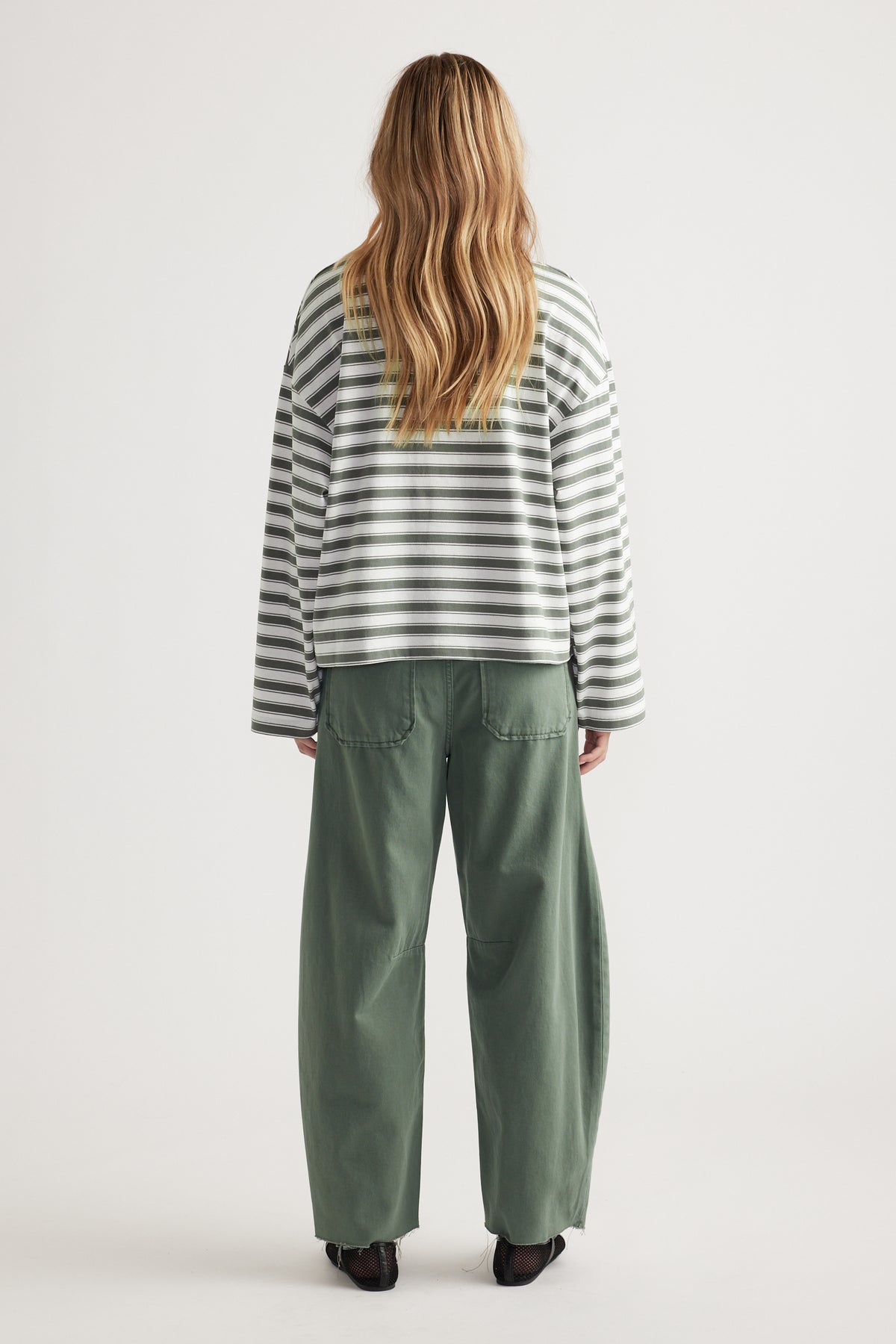Woman wearing relaxed fit green wide-leg pants and long sleeve white and grey striped tee seen from back