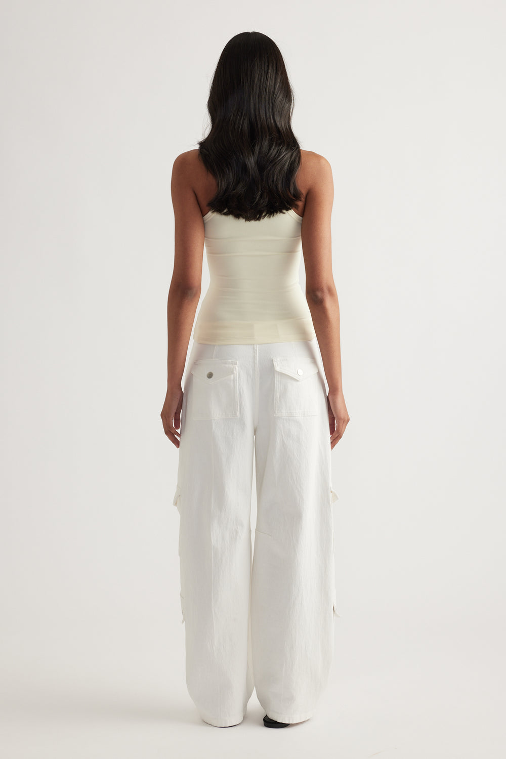 Model viewed from behind wearing a cream fitted tank top with white wide leg pants