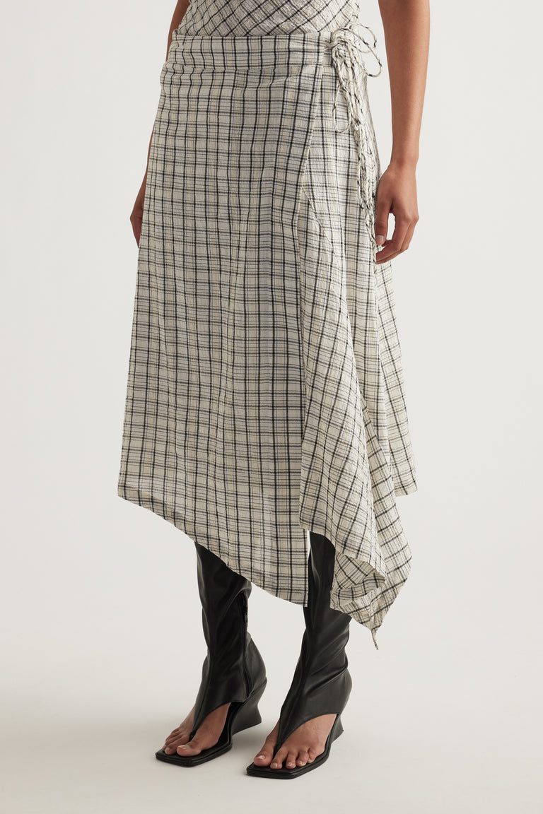 Woman wearing a checked wrap skirt with a tie waist, asymmetric handkerchief hem and black heeled sandals