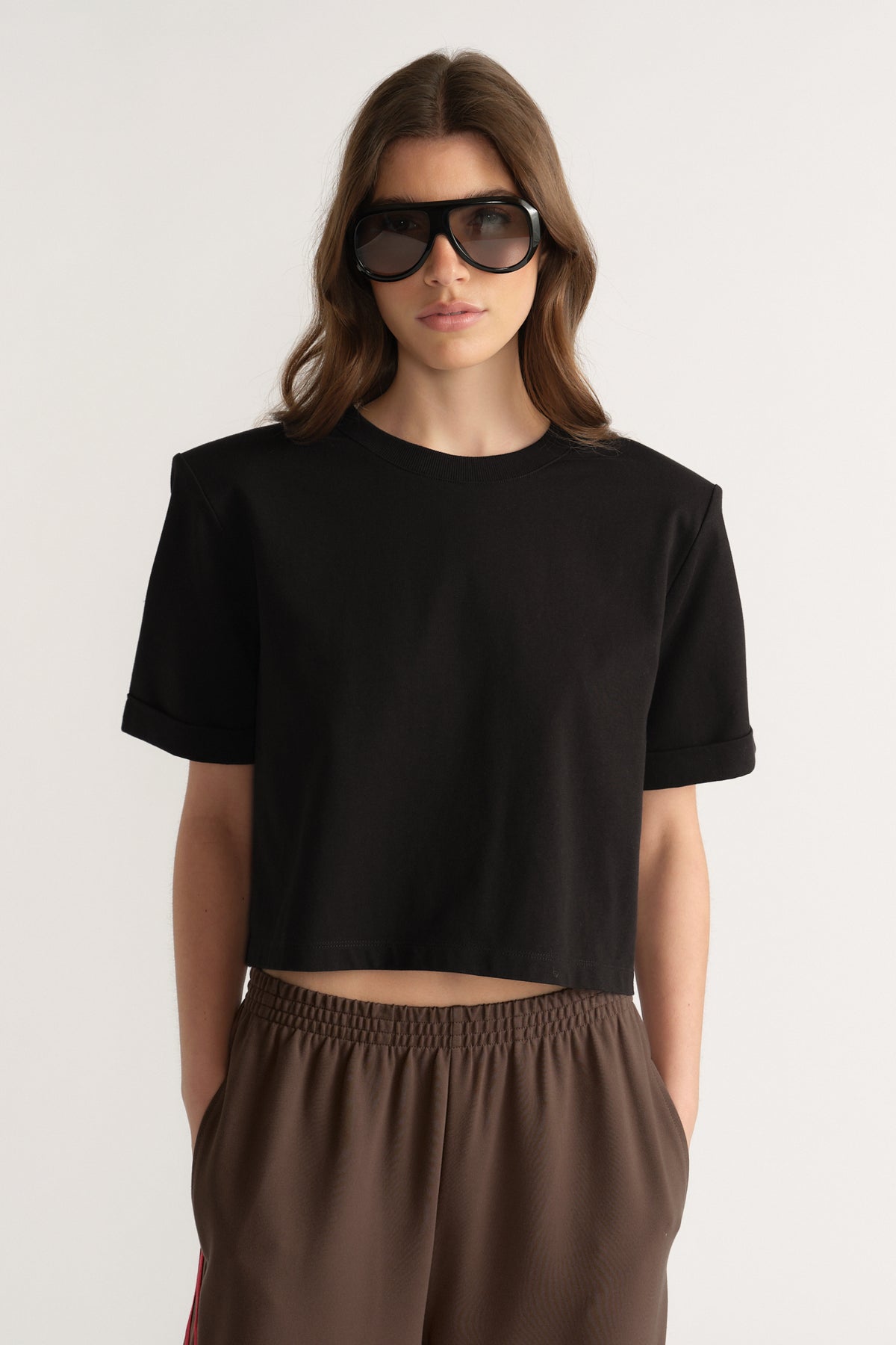 Woman wearing a black shoulder pad tee with brown pants and sunglasses