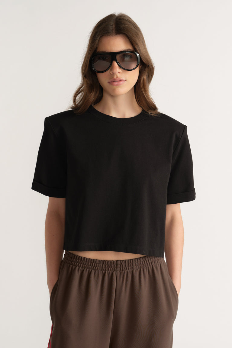 Woman wearing a black shoulder pad tee with brown pants and sunglasses