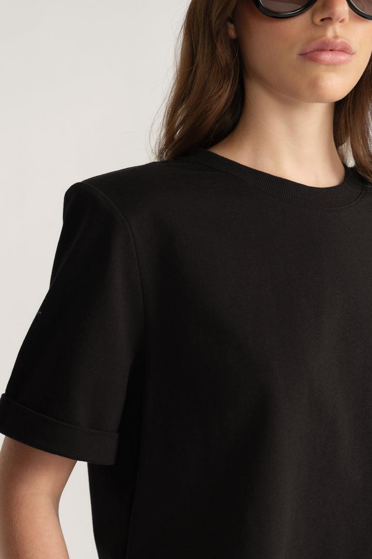 Woman wearing a black crew neck tee with structured shoulder pads and rolled sleeve cuffs