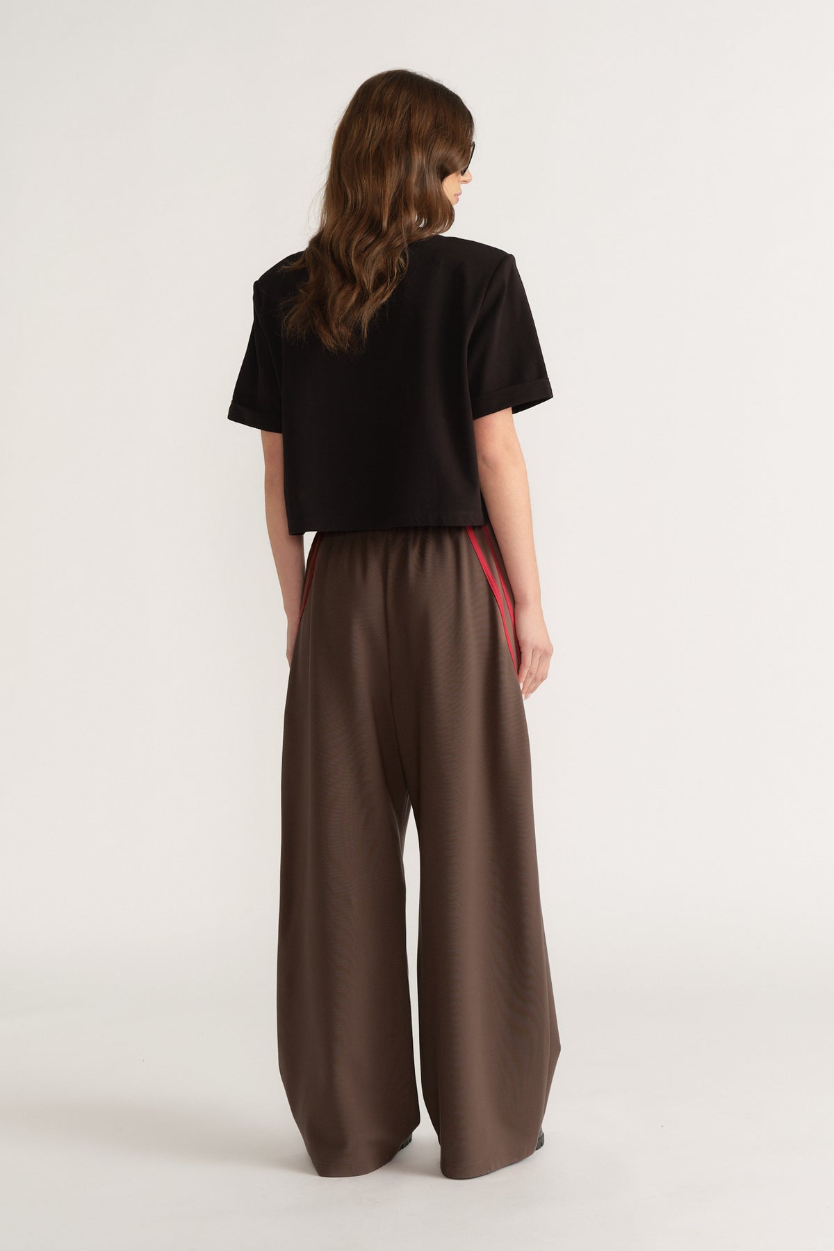 Back view of a woman wearing a black structured tee with brown wide leg pants and red side stripes