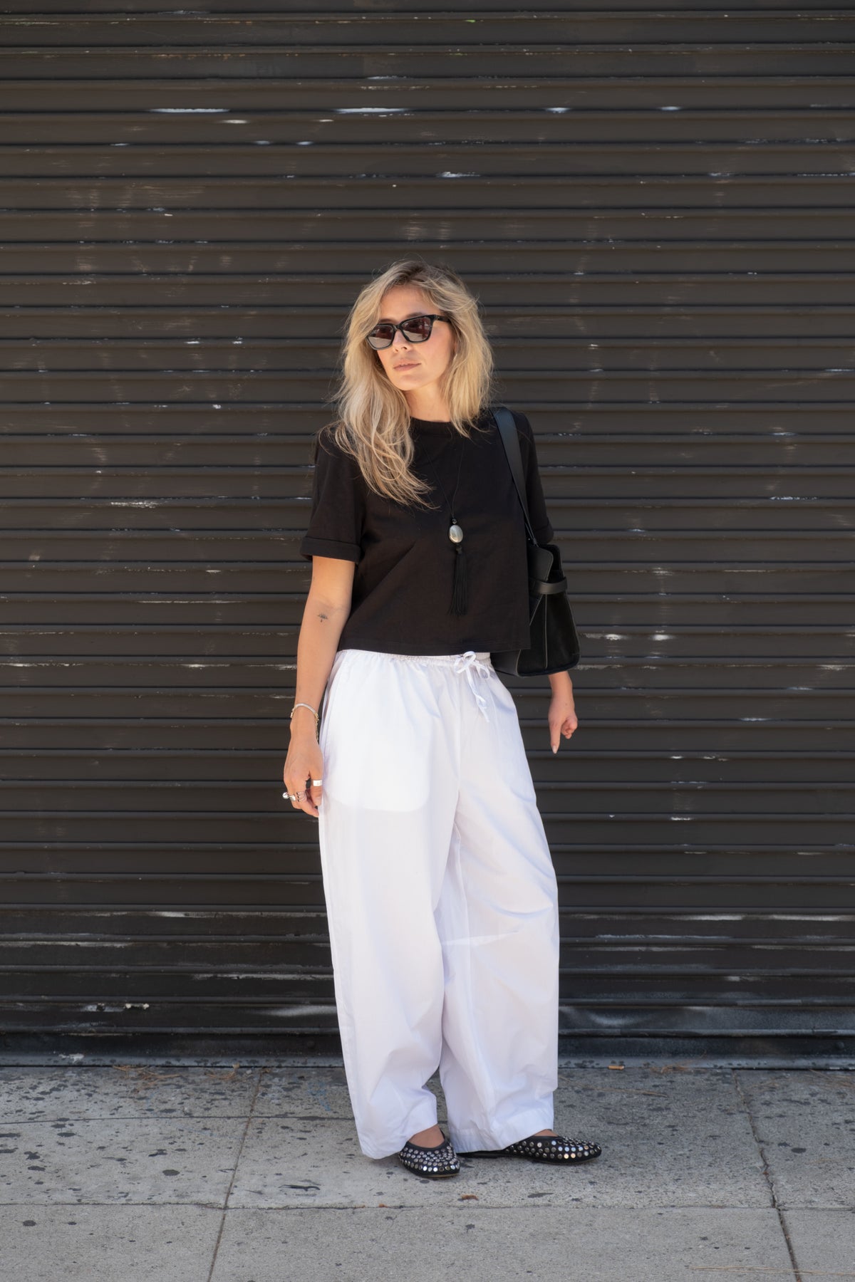 Woman in a black top and white barrel leg pants with sunglasses and studded flats