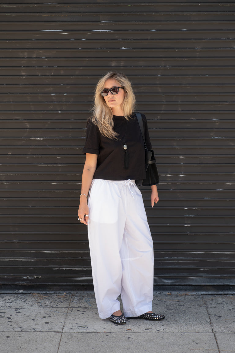Woman in a black top and white barrel leg pants with sunglasses and studded flats