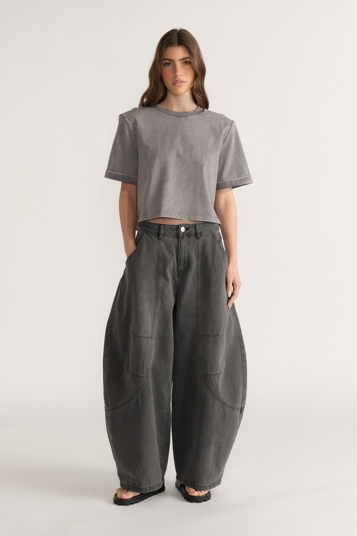 Woman wearing a grey structured shoulder pad tee with dark barrel leg pants and black sandals