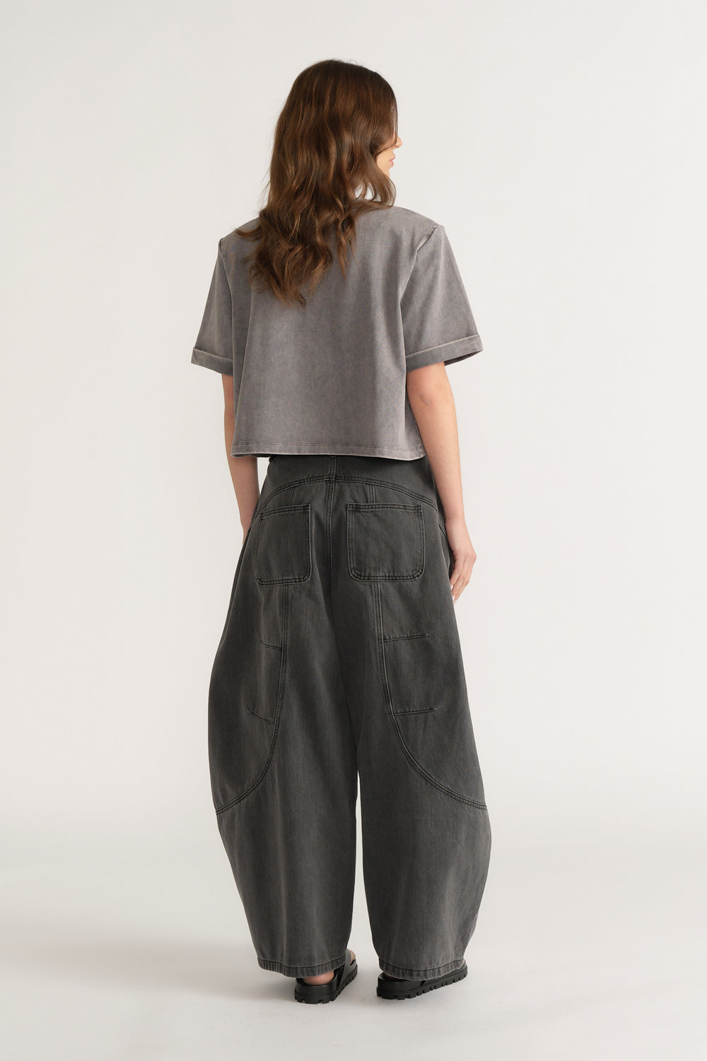 Woman seen from behind wearing a grey structured tee with dark barrel leg jeans and black shoes