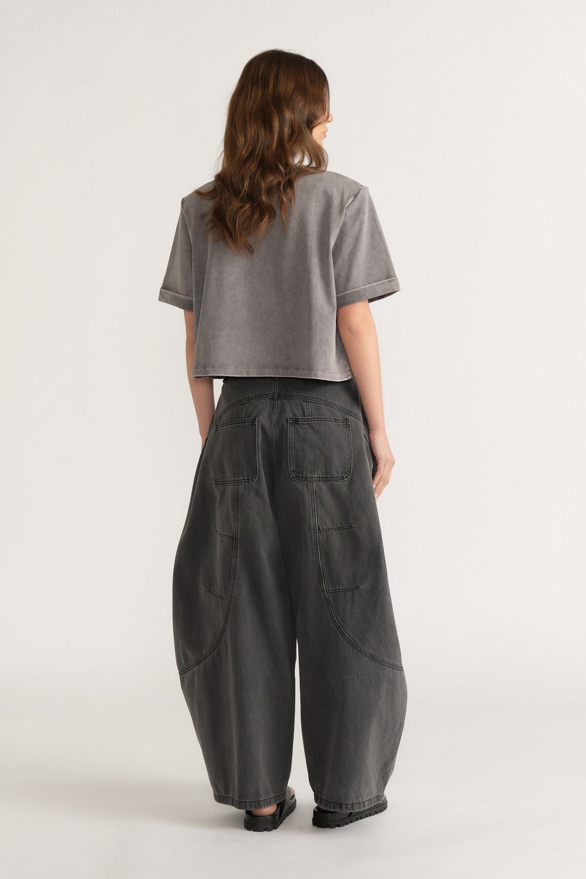 Woman seen from behind wearing a grey structured tee with dark barrel leg jeans and black shoes