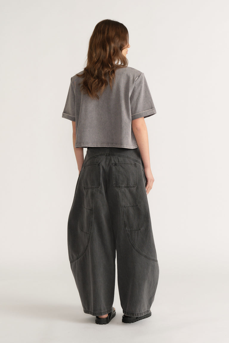 Woman seen from behind wearing a grey structured tee with dark barrel leg jeans and black shoes