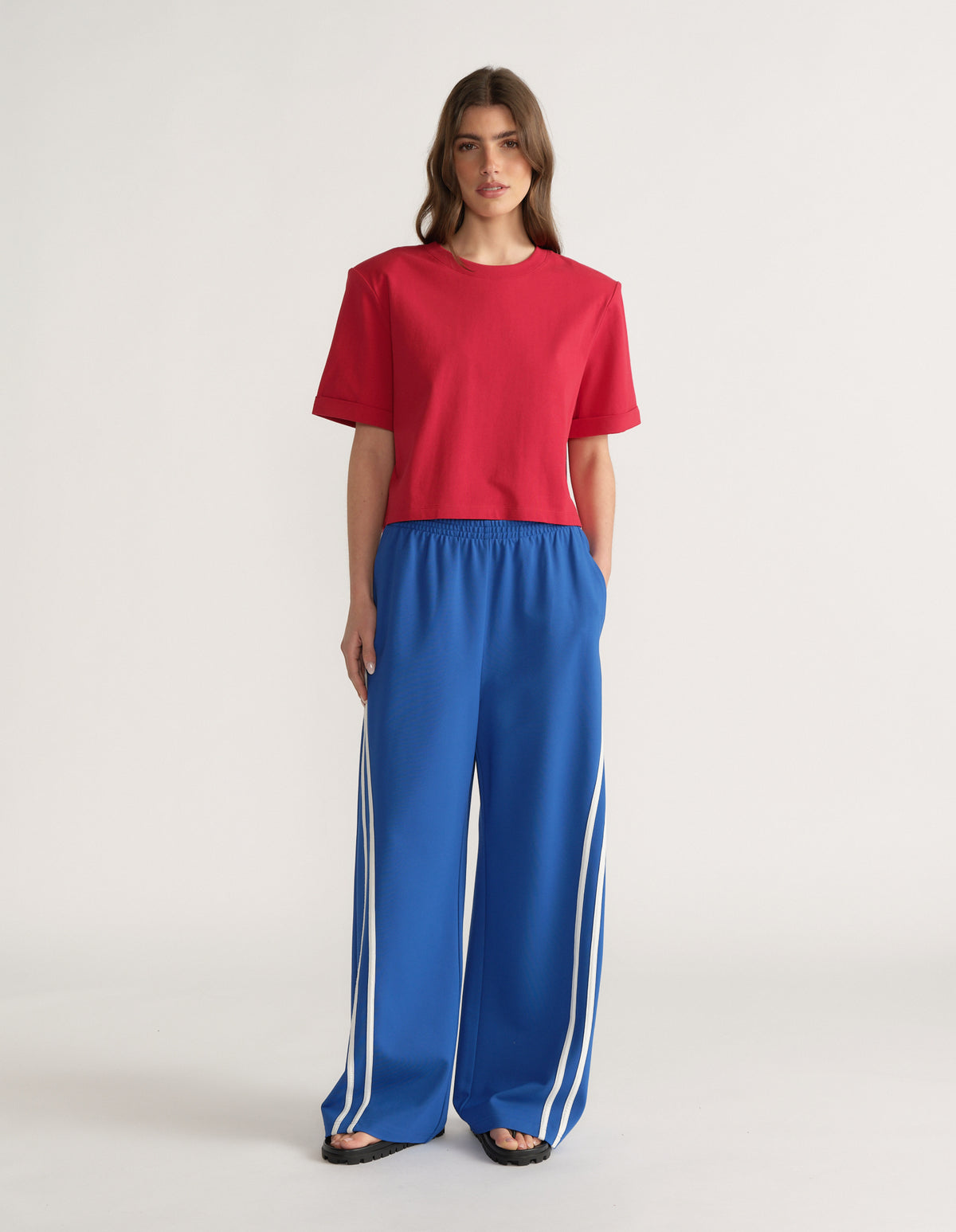 Woman wearing a red shoulder pad tee with blue wide leg track pants and white side stripes