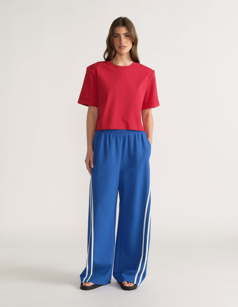 Woman wearing a red shoulder pad tee with blue wide leg track pants and white side stripes
