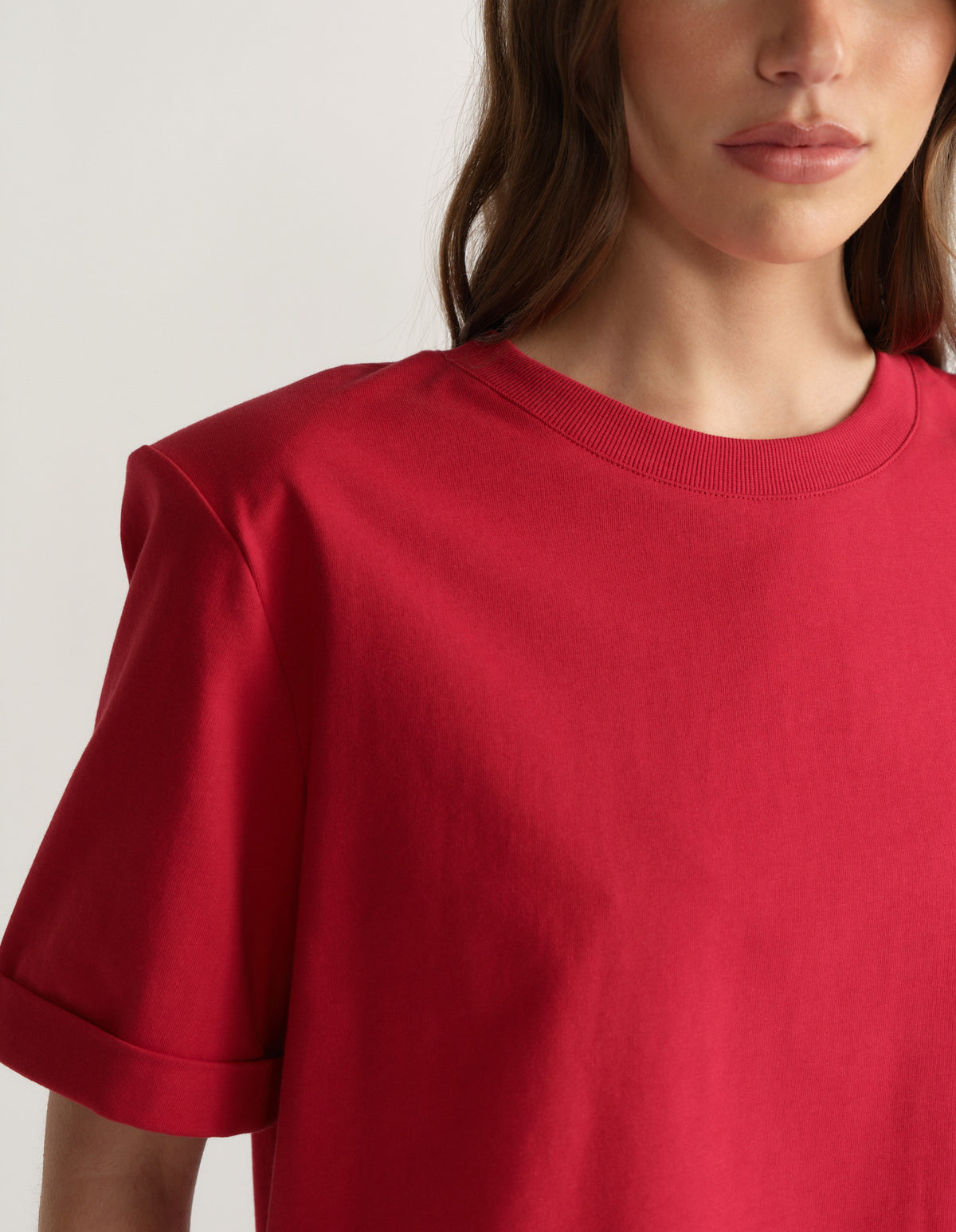 Woman wearing a red crew neck tee with padded shoulders and rolled short sleeves