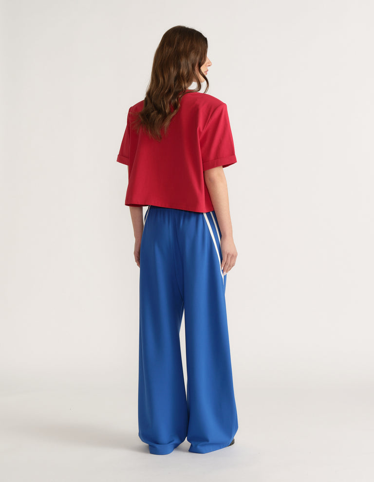 Woman viewed from behind wearing a red shoulder pad tee and blue wide leg pants