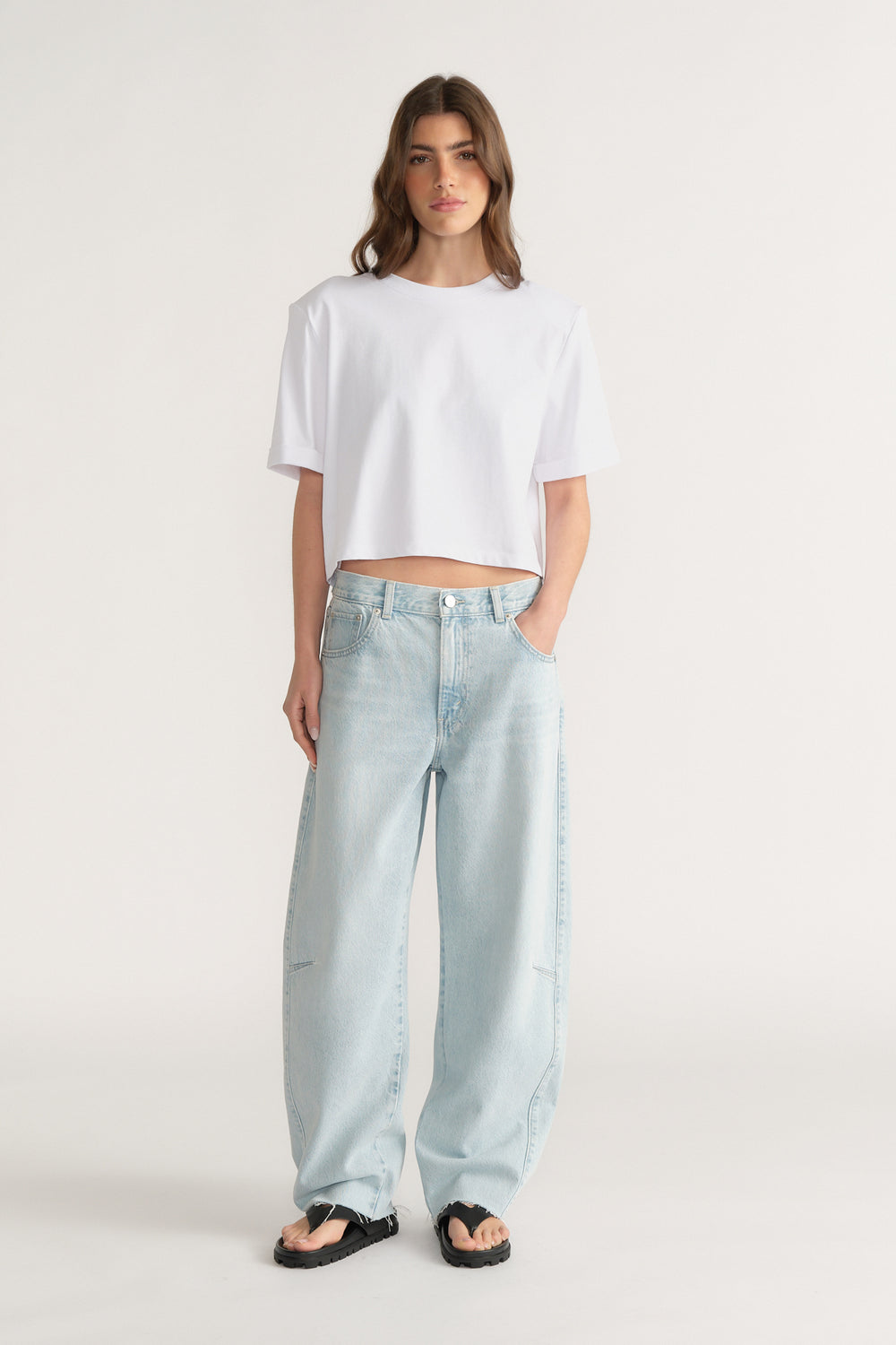 Woman wearing a cropped white shoulder pad tee with light blue wide leg jeans and black sandals