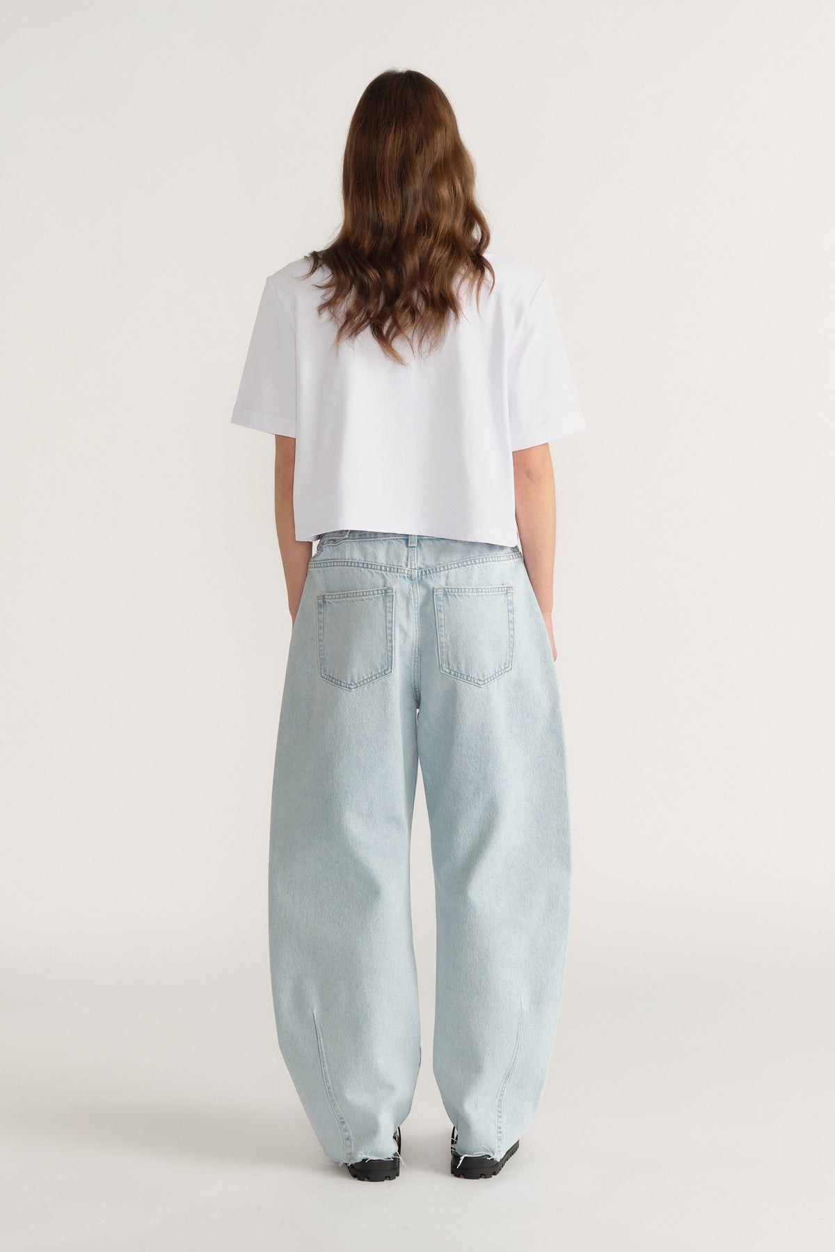 Back view of a woman wearing a white structured shoulder pad tee with relaxed light blue jeans