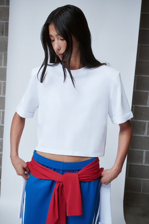 Woman wearing a white shoulder pad tee with blue pants and a red sweater tied at the waist