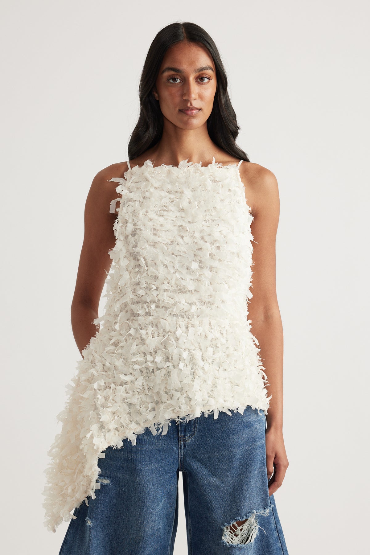 Woman wearing a white textured sleeveless asymmetric top with a square neckline and relaxed blue jeans
