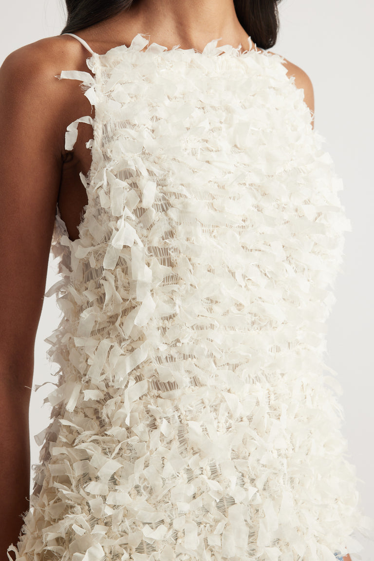 Woman wearing a white textured sleeveless top with thin straps and an asymmetrical hem