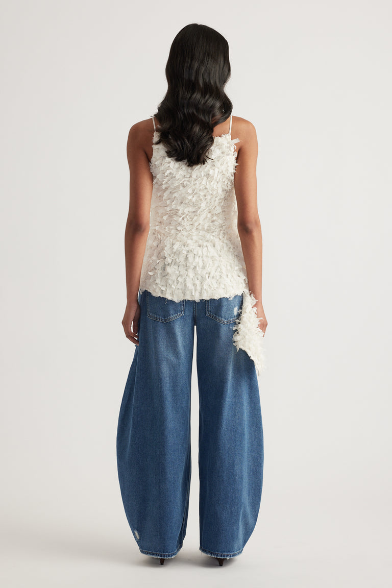 Back view of a woman wearing a white textured sleeveless top with an asymmetric hem and wide leg blue jeans