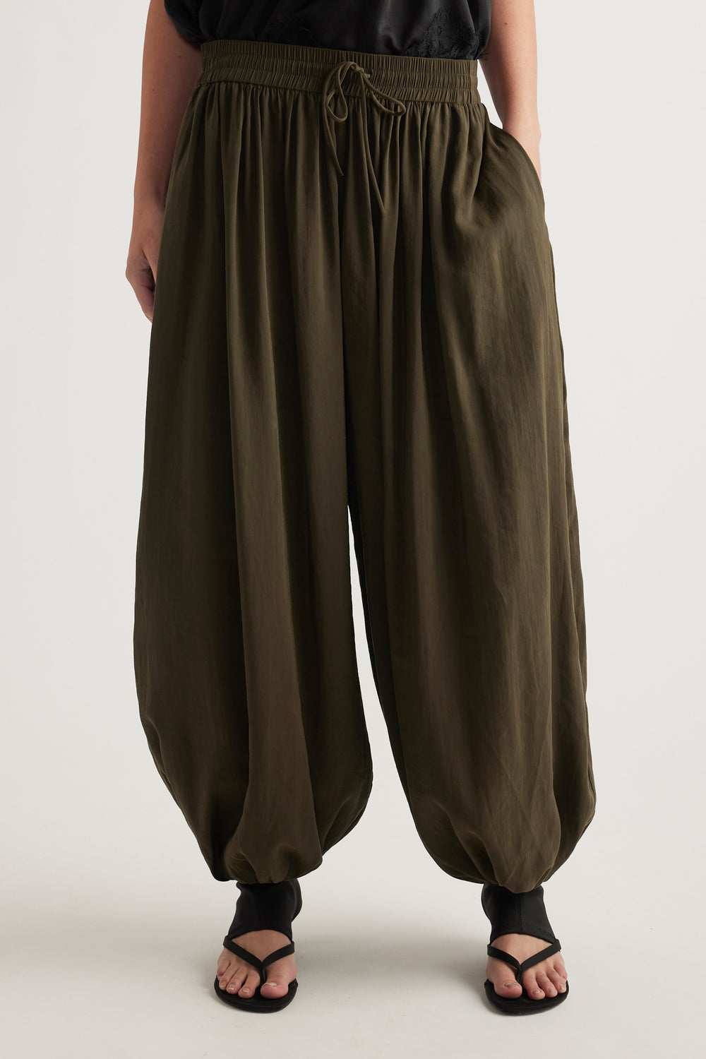 Woman wearing olive green balloon leg pants with an elastic drawstring waist and gathered cuffs