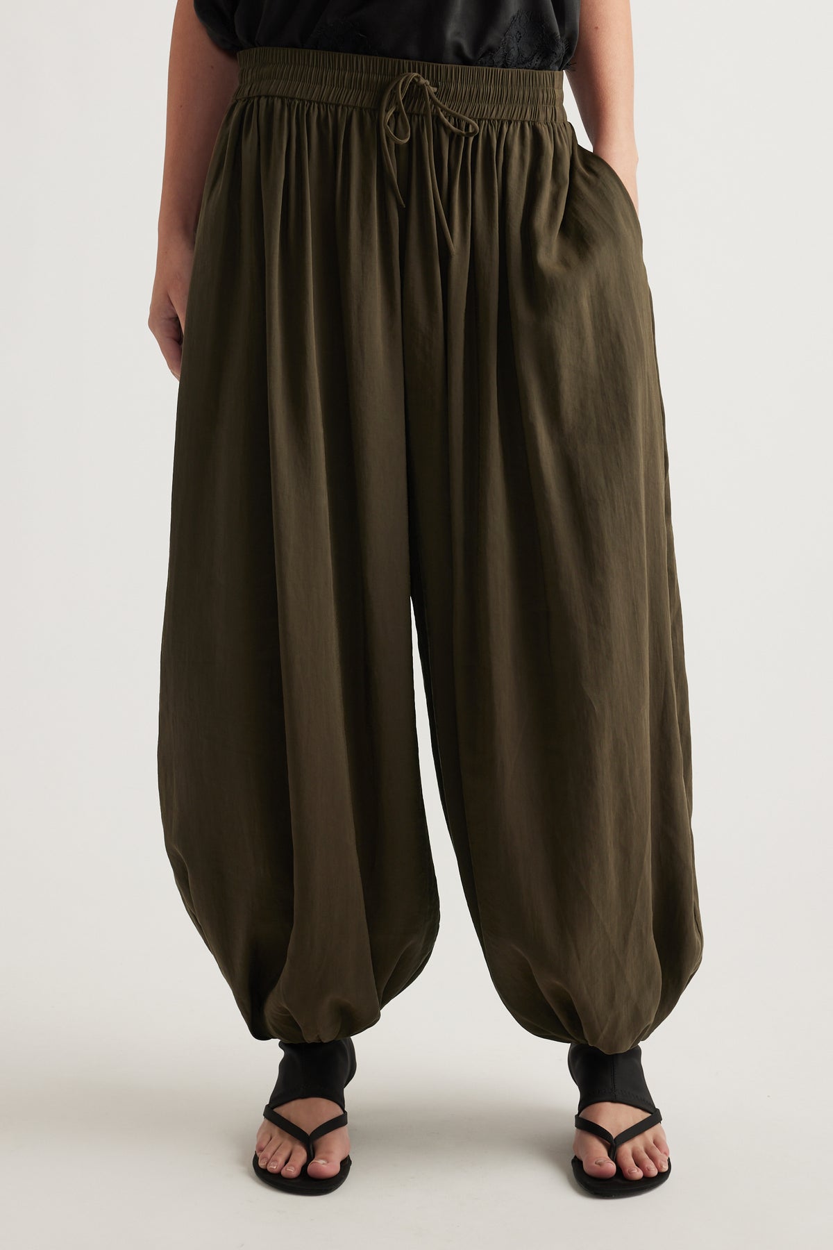 Woman wearing olive green balloon leg pants with an elastic drawstring waist and gathered cuffs