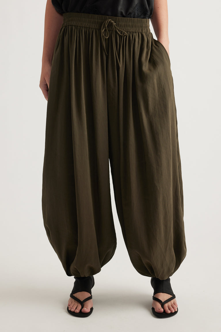 Woman wearing olive green balloon leg pants with an elastic drawstring waist and gathered cuffs