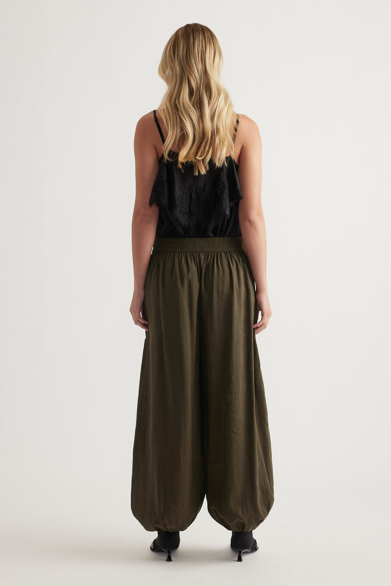 Woman viewed from behind wearing olive balloon leg pants with an elastic waist, black top and heels