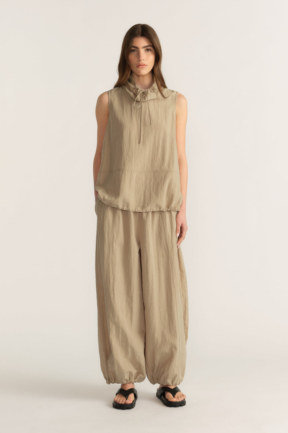 Woman wearing a beige sleeveless tie neck top with matching relaxed balloon pants and sandals