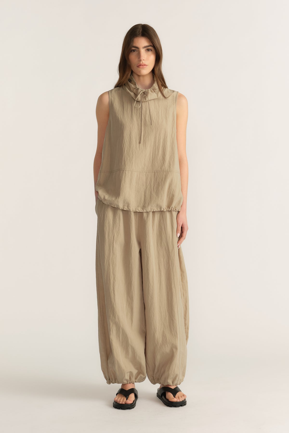 Woman wearing a beige sleeveless tie neck top with matching relaxed balloon pants and sandals