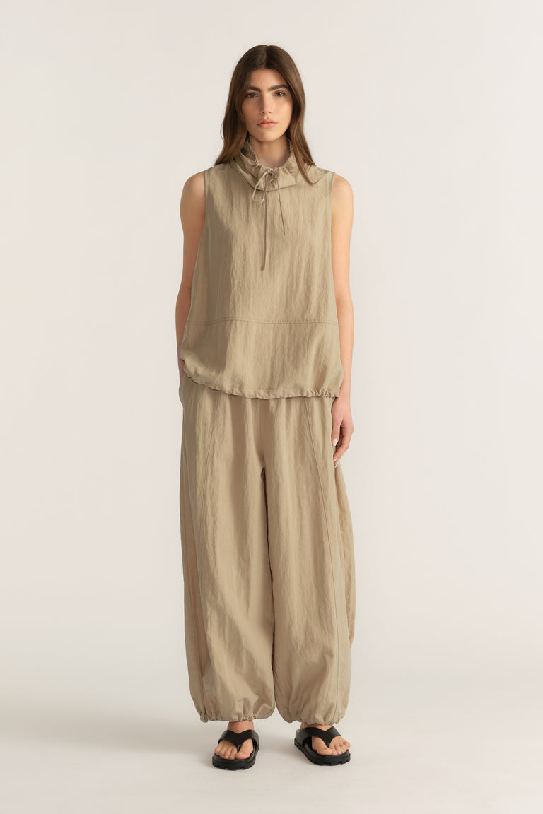 Woman wearing a beige sleeveless tie neck top with matching relaxed balloon pants and sandals
