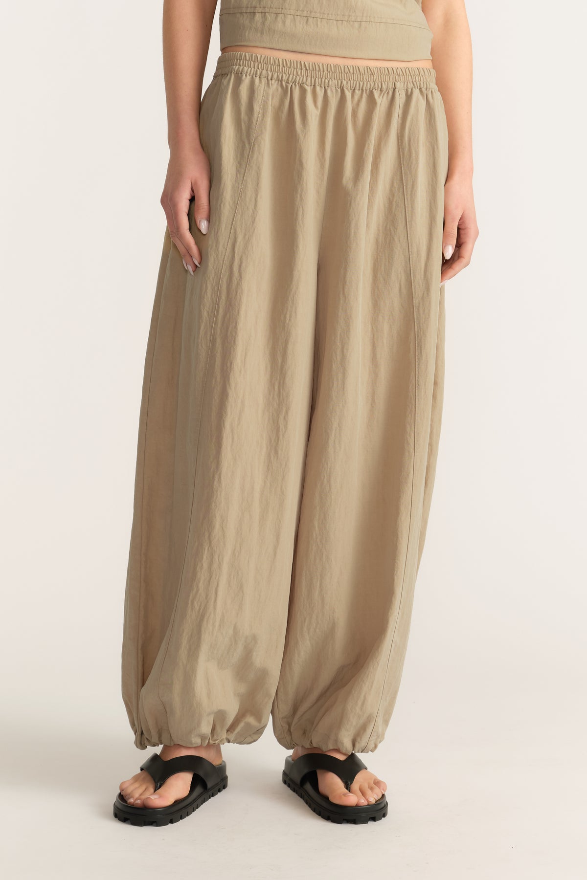 Woman wearing beige ankle-length balloon pants with an elasticated waist and gathered hems